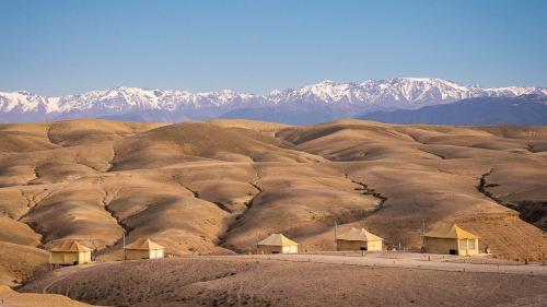 Eine Ansammlung von Hütten in einer Wüste mit schneebedeckten Bergen in der Unterkunft Agafay Luxury camp in Marrakesch