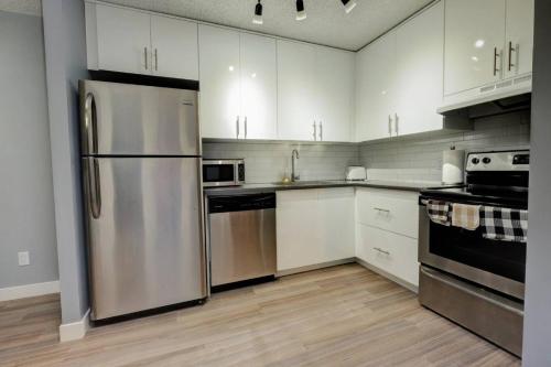 a kitchen with white cabinets and a stainless steel refrigerator at Stylish DT Condo ~2 Blocks from Stampede Grounds in Calgary