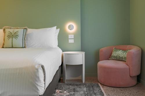 a bedroom with a bed and a pink chair at Victoria Street Boutique Hotel Townsville in Townsville