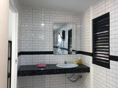 a white tiled bathroom with a sink and a mirror at Lanta Vacation House in Ko Lanta