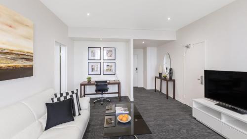a living room with a white couch and a tv at Flagstaff Gardens Hotel Melbourne in Melbourne