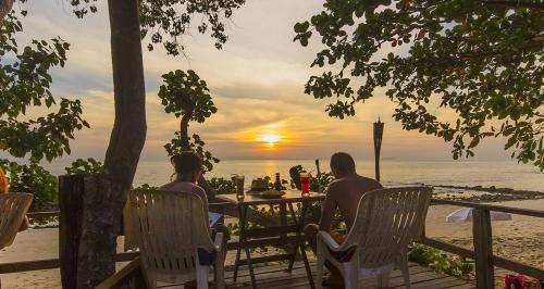 俊島的住宿－裕姆島度假村，两人坐在海滩的桌子上,欣赏日落