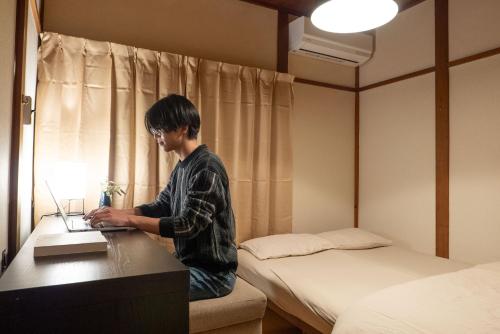 a man sitting at a desk with a laptop at Guest House KITOEDA in Nikko