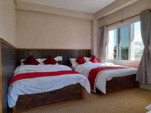 a bedroom with two beds with red pillows and a window at Hotel Himalayan Vista in Pāti Bhanjyāng