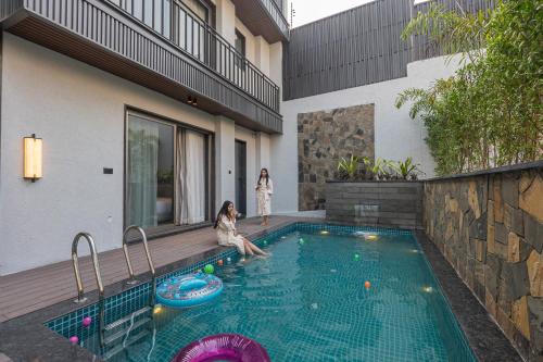 a woman sitting in a swimming pool next to a house at SaffronStays Boudhi Tree Villas in Rishīkesh