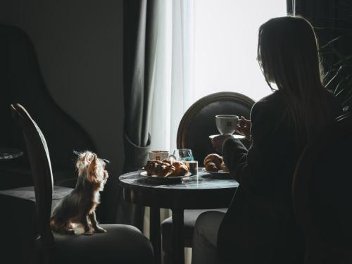 eine Frau, die mit einem Hund an einem Tisch sitzt und aus dem Fenster schaut in der Unterkunft Locanda Sibilla Luxury Suites in Tivoli