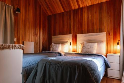 two beds in a room with wooden walls at Cabañas Punto Prana in Tandil