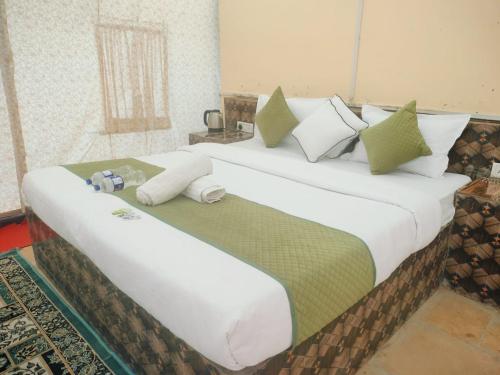a large bed with white sheets and green pillows at Raj Kesari Heritage Camp in Jaisalmer