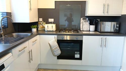 a kitchen with white cabinets and a black oven at Stylish Seaside Cottage - 3 minute walk to beach with parking in Skegness