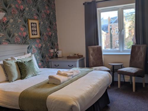 a bedroom with a bed with two chairs and a window at Hitchin Priory Inn in Hitchin