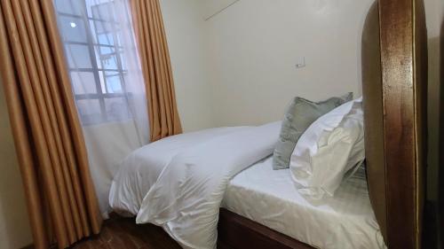 a bed with white sheets and pillows next to a window at Coral Homes in Juja