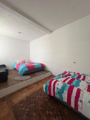 two beds in a room with white walls and wooden floors at Hostal Los Robles in Pasto