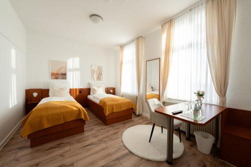 a bedroom with two beds and a desk and a table at Hotel Mutter Buermann Hannover in Hemmingen