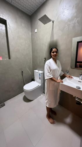 a woman standing in a bathroom with a sink and a toilet at Lucky Wave Beach Resort in Colombo