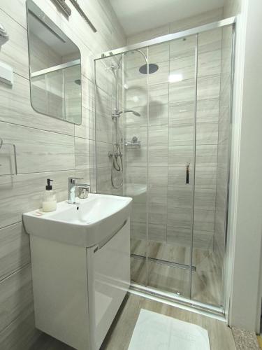a white bathroom with a shower and a sink at TOKIs apartmani in Mrkonjić Grad