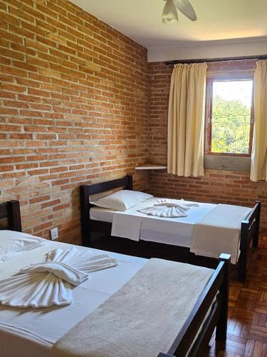 a room with two beds and a brick wall at Pousada Siloé - Mosteiro de São Bento em Vinhedo in Vinhedo