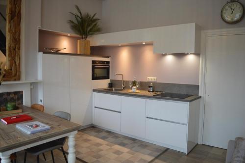 een keuken met witte kasten en een tafel en een klok bij Logeren aan de Haven - Appartement Spijkerbrug in Middelburg