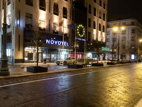 eine Stadtstraße bei Nacht mit Gebäuden und einem Auto in der Unterkunft Novotel Vilnius Centre in Vilnius