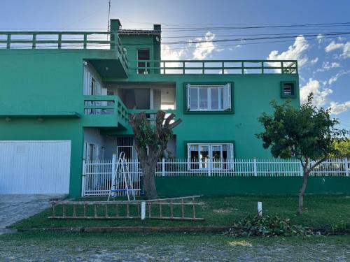 a green house with a white fence in front of it at Apartamentos Mobiliados em Imbé in Imbé
