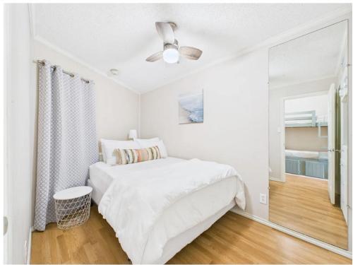a white bedroom with a bed and a ceiling fan at Galveston condo- walk to beach - ocean view - 2 pools in Galveston