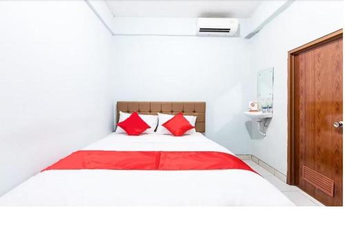 a white bedroom with a bed with red pillows at Hotel Cemara Gading in Bubulak 3