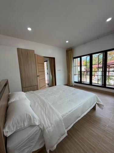 a large white bed in a bedroom with windows at Bancha white house in Ban Bo Han