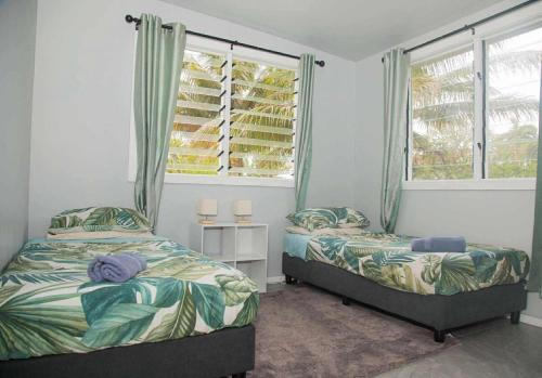 two beds in a bedroom with two windows at 2 Bedroom House - Villa Teremoana in Ngatangiia