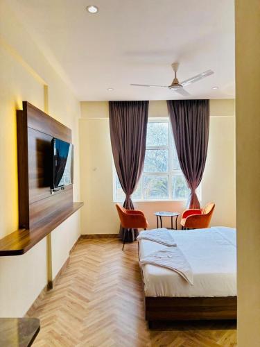 a bedroom with a bed and two chairs and a tv at Hotel Nirmal's Executive in Pune