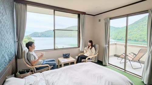a man and woman sitting in a hotel room with windows at H,U,B Unzen - Vacation STAY 01672v in Unzen