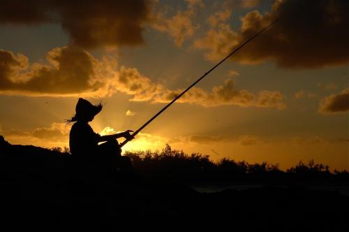 a person is holding a fishing rod at sunset at Baia Sonambula in Praia do Tofo