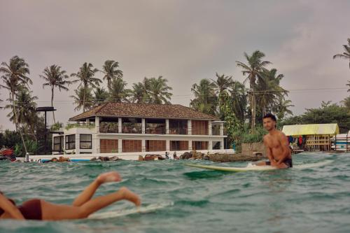 a man standing on a surfboard in the water at UNU Boutique Hotel -- Adults Only -- in Ahangama