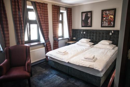 a bedroom with a bed and a chair and windows at Apartamenty Siedem Komnat Siedmiu Mistrzów in Toruń