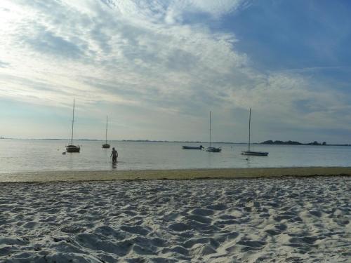 a person standing in the water on a beach with sailboats at Haus Achtern Diek in erster Reihe am Meer in Fehmarn