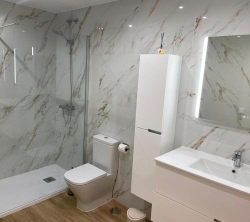 a white bathroom with a toilet and a sink at Apartamentos Ézaro Beach in Dumbría