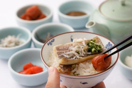 a person holding a bowl of rice with food at Hotel New Tsuruta in Beppu