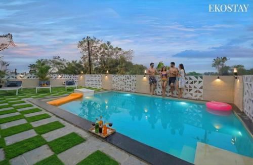 a group of people standing on a fence near a swimming pool at EKOSTAY - Alpine Villa in Alibaug