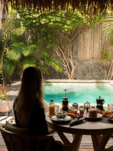 eine Frau sitzt mit Essen an einem Tisch vor einem Pool in der Unterkunft Villa Palma Gili Meno - Private Pool - Adult Only in Gili Meno