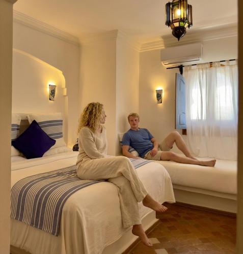 a man and woman sitting on beds in a hotel room at Hotel Al Alba Hammam & Restaurant in Asilah