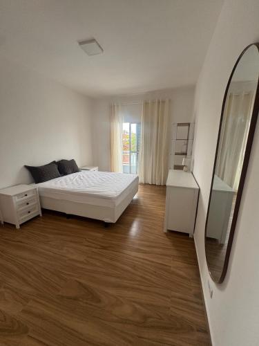 a white bedroom with a bed and a mirror at Casa beira Mar in Itanhaém