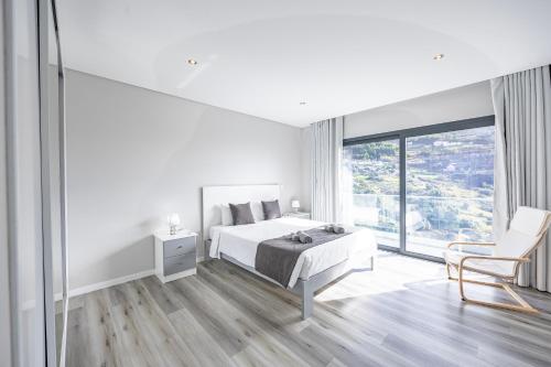 a white bedroom with a bed and a chair at Paradise Pereira House BY YOUR KEY MADEIRA in Calheta