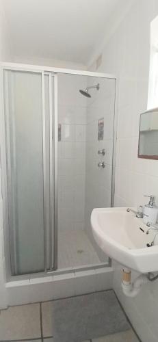 a white bathroom with a shower and a sink at Shark Cove Little Cottage in Kleinbaai