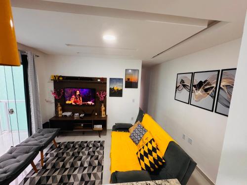 een woonkamer met een gele bank en een tv bij Ap 800m da praia in Rio das Ostras
