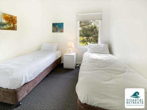 two beds in a room with a window at Phillip Island Villa - Phillip Island Resort in Cowes