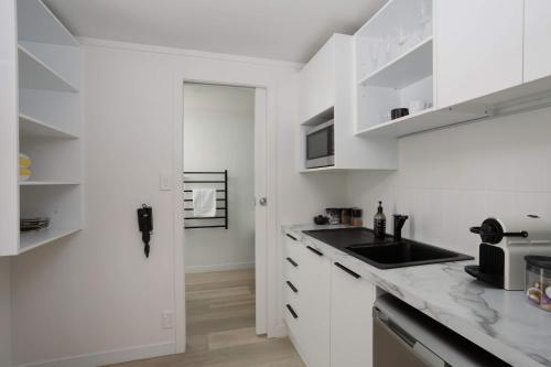 a white kitchen with white cabinets and a sink at Spacious, Breezy Studio Apartment, Moments from Downtown and Beach in Mount Maunganui