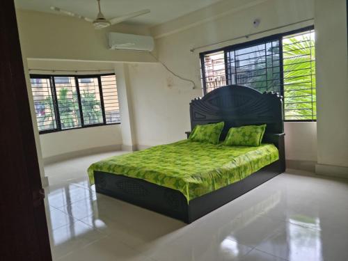 una camera da letto con un letto verde con due finestre di M Ali House a Sylhet