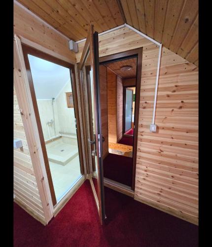 a small wooden room with a door and a mirror at Casa Albiony Dâmbovicioara in Dâmbovicioara
