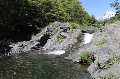 un ruscello d'acqua con una montagna sullo sfondo di Vista al volcán con tinaja y río en Conguillío a Curacautín