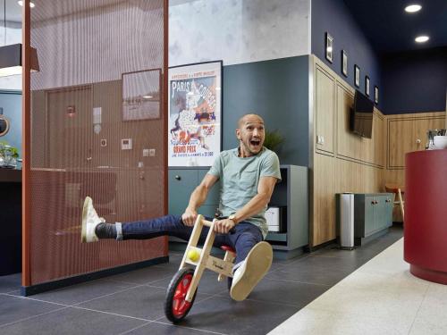 een man zit op een driewieler in een kamer bij Aparthotel Adagio Paris Suresnes Longchamp in Suresnes