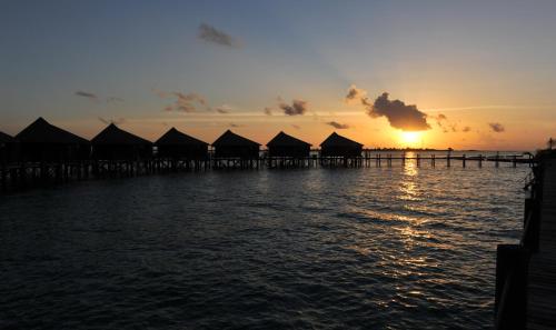 a sunset over a pier with huts on the water at Komandoo Island Resort & Spa in Komandoo