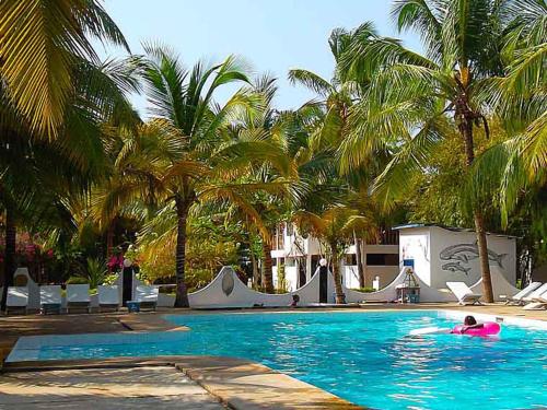 a person swimming in a swimming pool with palm trees at Hotel Village Vacances Awale Plage in Grand-Popo